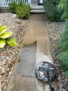 A professional surface cleaner power washing a dirty concrete sidewalk, removing dark grime and restoring the original color in Huron Ohio.